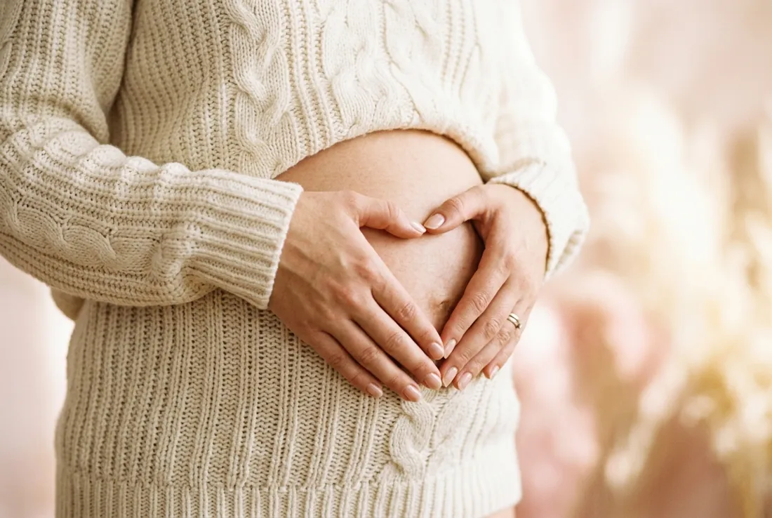 Second Trimester: The Golden Weeks Pregnant belly with hands forming a heart shape in cozy cream sweater